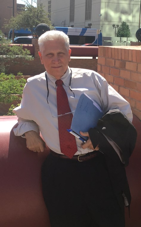 Alex Lieber-Alessie, attorney, in a shirt and tie, holding case papers and a jacket